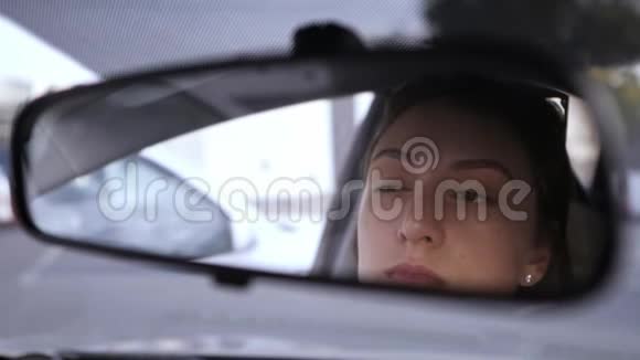 一个漂亮的白人女孩看着汽车的后视镜把阴影放在她的眼睛上违反法律视频的预览图