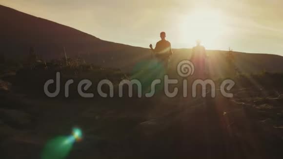 一个男人和一个女人带着背包和徒步旅行棒的剪影沿着走在阳光下视频的预览图