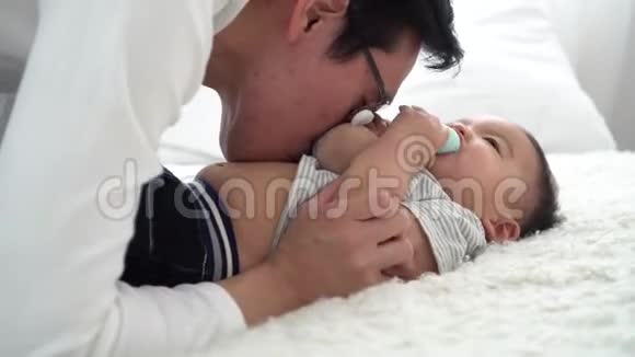 一家年轻的亚洲父亲和他的妻子温柔地亲吻他的小男孩的肚子视频的预览图