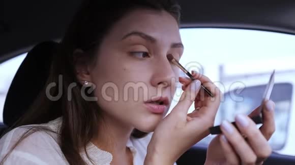 女商人在车里化妆的肖像用刷子涂抹眼影女孩进入眼睛和胜利视频的预览图