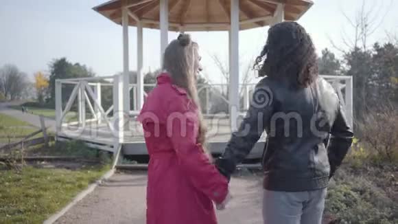 积极的两族青年夫妇站在秋天公园的亭子前笑着说话快乐的嬉皮士视频的预览图