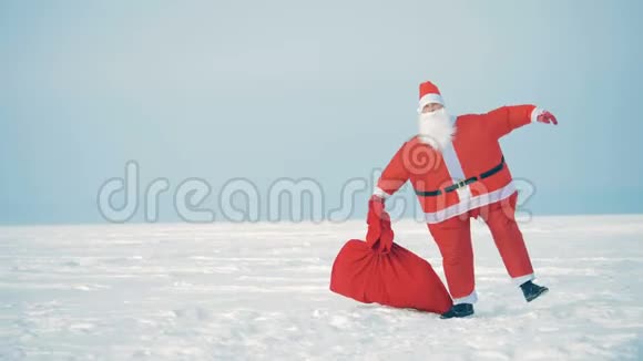 圣诞老人手里拿着一袋礼物他嘲笑自己在雪地里跳跃视频的预览图