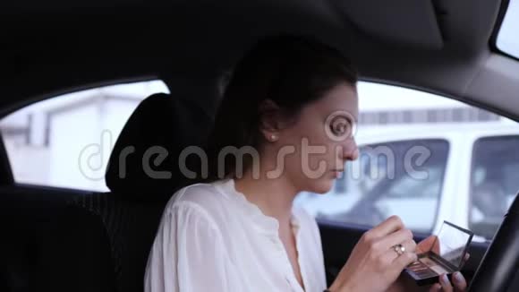 在车里化妆一位年轻貌美的女子穿着一件白色上衣在画笔上吹着眼影的肖像视频的预览图