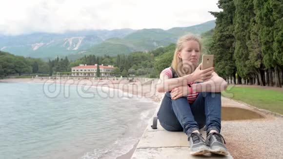 漂亮的年轻女娃娃坐在带智能手机的栏杆上视频的预览图