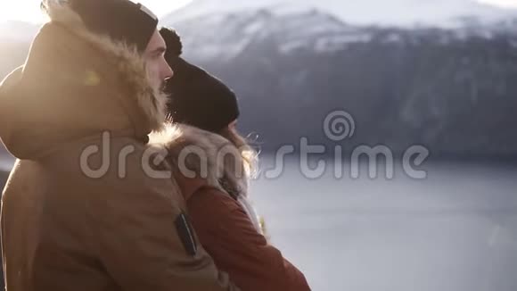 年轻夫妇穿着冬装拥抱人们拥抱着看着美丽的湖泊和山峰赞赏视频的预览图
