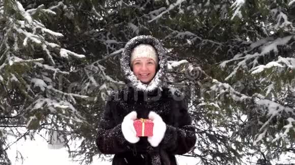 幸福微笑的女人送红色的礼物盒站在白雪皑皑的公园里视频的预览图