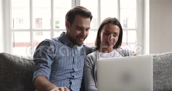 快乐的年轻夫妇用笔记本电脑坐在沙发上聊天视频的预览图