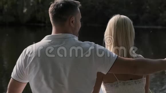 年轻的恋人坐在河边的码头上亲吻背面视频的预览图