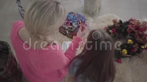 金色的成年女性和深色的小女孩坐在柔软的地毯上选择装饰母亲和视频的预览图