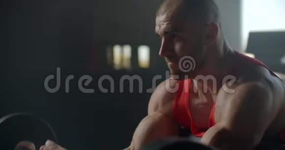 力量训练臂肱二头肌配杠铃身材苗条肌肉发达的男人举起一个杠铃坐在健身房里视频的预览图
