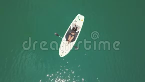 空中拍摄蓝色海面上躺在桨板上的性感黑发女人的后景视频的预览图