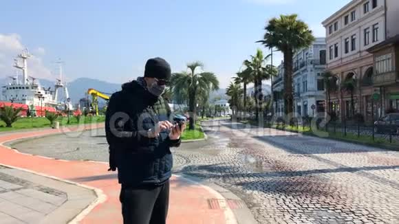 街上戴面式医疗面具的男子使用智能手机视频的预览图