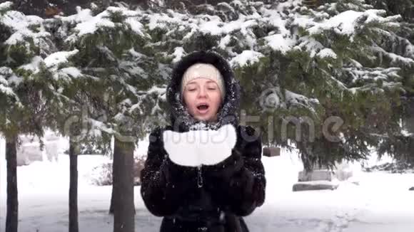 美丽的快乐女孩在霜冬公园吹雪花的肖像视频的预览图