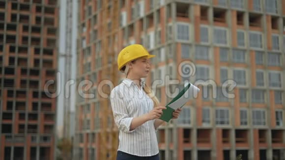 一个戴着安全帽的建筑工地上的女建筑师手里拿着一块平板电脑手里拿着一计划的文件视频的预览图