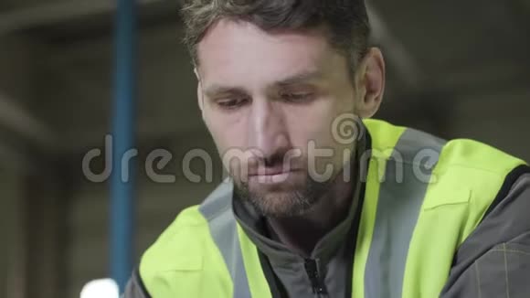 一幅严肃的白种人的特写肖像身穿绿色背心俯视着在制造厂工作的专业工人视频的预览图