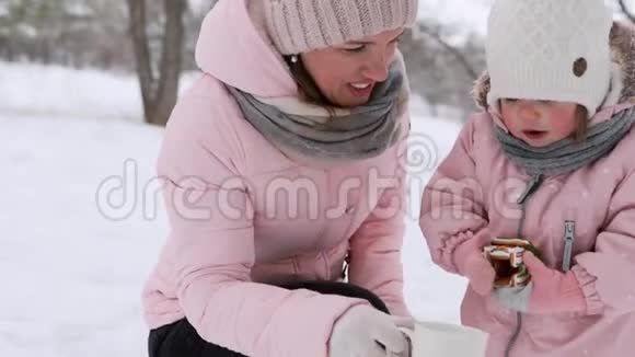 母女俩在冬林喝热暖茶可爱的女孩和快乐的母亲拿着茶杯和圣诞节视频的预览图