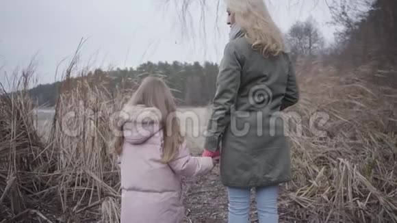 在湖或河前的秋天灌木丛中一位成年金发女子和一位棕色小女孩的后景高加索人视频的预览图