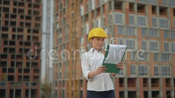 一个戴着安全帽的建筑工地上的女工程师手里拿着一块写字板一个纸托上面有一个视频的预览图