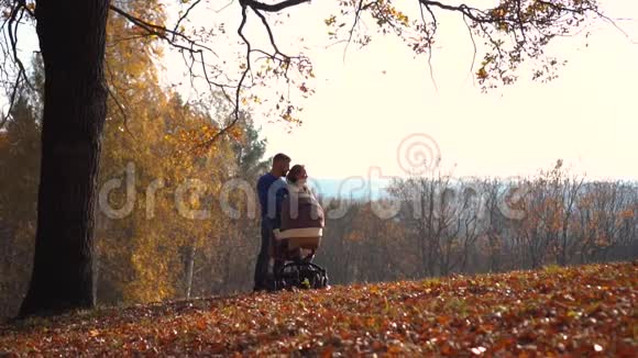 年轻的家庭站在秋天的树叶下视频的预览图
