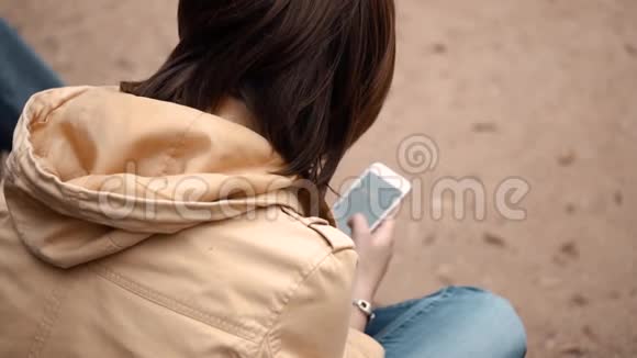 一个年轻女孩独自坐在公园里拿着电话视频的预览图