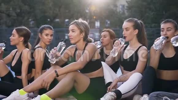 身材苗条的运动型健身妇女坐在室外体育场地板上在运动锻炼后喝水视频的预览图