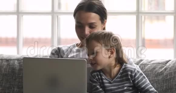 妈妈教可爱的儿子用笔记本电脑坐在沙发上视频的预览图