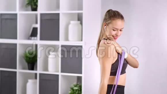 微笑健身妇女用橡皮筋在家中中弹训练肩部肌肉视频的预览图