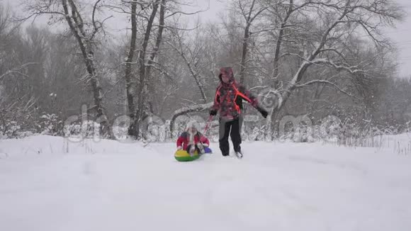 爸爸在降雪的冬季森林里骑着他的女儿在雪橇上快乐的父母在圣诞节和孩子玩视频的预览图