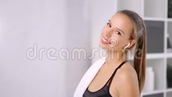 戴着耳机的健康微笑女人在白色房间内摆姿势看镜头的肖像视频的预览图