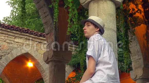 在一个美丽浪漫的花园里一个悲伤的少年站在罗马圆柱旁视频的预览图