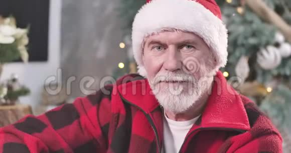 一位戴着红色圣诞帽的白种人老人的特写肖像看着摄像机眨眼正面圣诞老人摆姿势视频的预览图