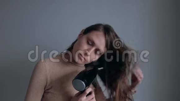 漂亮的女人用黑色吹风机在白色的墙壁背景上烘干头发视频的预览图