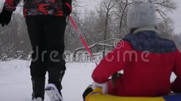爸爸和妈妈在冬天的森林里骑着他们的女儿的雪橇快乐的父母和他们的孩子在圣诞公园玩视频的预览图