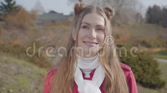 年轻白种人女人看镜头微笑的肖像站在秋天公园的金发美女快乐的嬉皮士视频的预览图