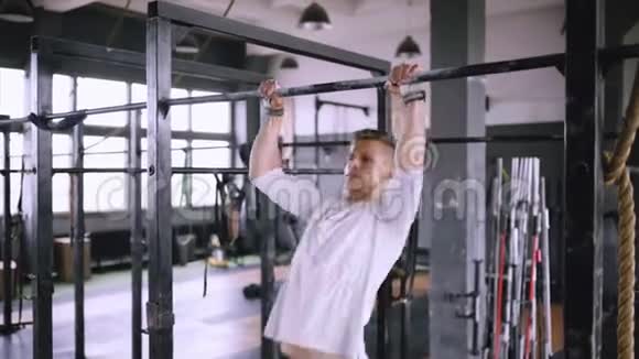 一个男人在健身房的酒吧里停下来穿着提拉和抓握的装备和白色t恤视频的预览图