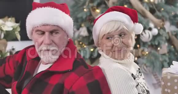 快乐成熟的白种人夫妇背靠背坐着看着镜头微笑着圣诞节新年视频的预览图
