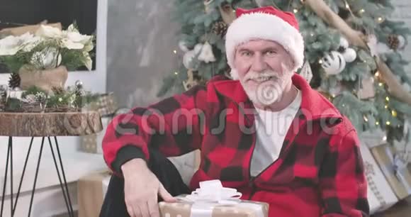 成熟的白种人坐在新年树的背景下带着礼物和微笑的肖像快乐的老家伙视频的预览图