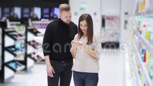 化妆品店里的丈夫和妻子看着智能手机聊天视频的预览图