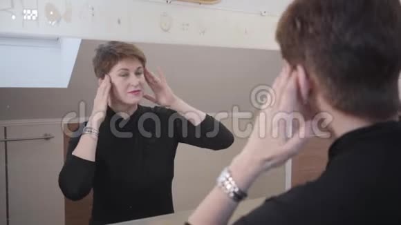 在迷人的深褐色头发的女士的镜子里拍摄反射的肩膀高加索女人摸着她的脸视频的预览图
