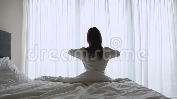 年轻女子伸展着身体醒来时坐在床上动作缓慢视频的预览图