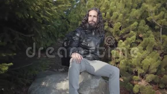 自信英俊的中东男人坐在树间的岩石上望着远处的肖像年轻的嬉皮士视频的预览图