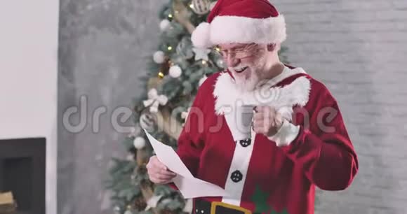 微笑着穿着圣诞老人服装的老白种人喝着咖啡读着信戴着眼镜的圣诞老人微笑着视频的预览图
