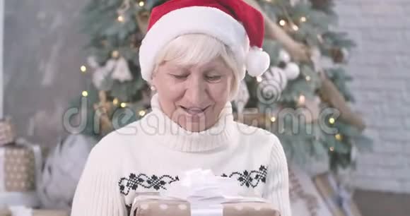 满脸惊讶的成熟白种人女人拿着圣诞礼物盒看着相机微笑着可爱的女士视频的预览图