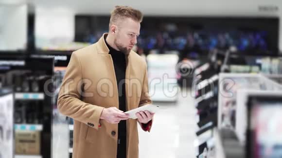 穿棕色外套的年轻帅哥在化妆品店里用数码平板电脑视频的预览图