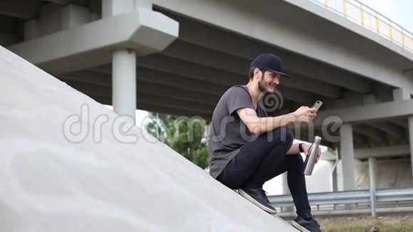 年轻人坐在桥下手里拿着智能手机和钢瓶视频的预览图