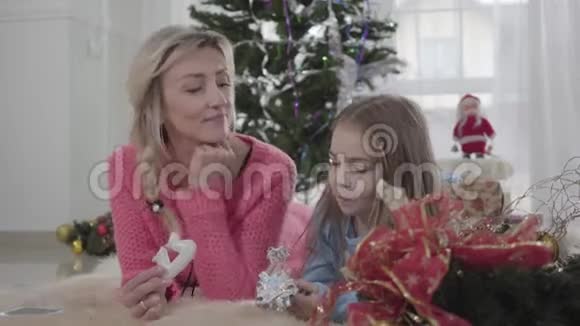 快乐白人母女躺在地板上吃饼干的肖像快乐的妈妈听着她的孩子视频的预览图