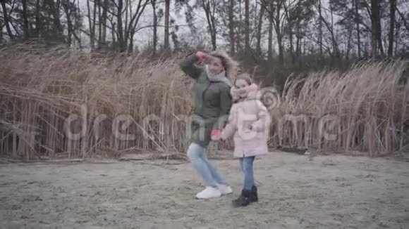 微笑的白种人女人的肖像手牵着额头和她的女儿说话快乐的女孩跳跃视频的预览图