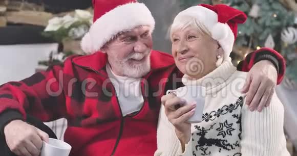 一对积极的老白种人夫妇在圣诞树的背景下喝咖啡和交谈快乐的男人视频的预览图