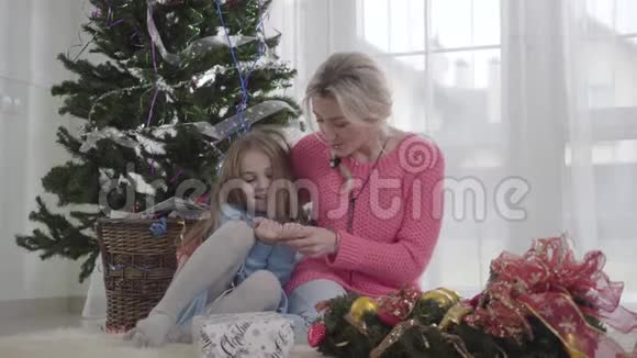 在圣诞树的背景下和成年女人坐在一起的白人女孩微笑妈妈和她的孩子说话视频的预览图