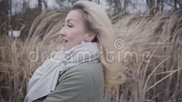 站在风中的迷人年轻女子的侧视白种人金发女孩在户外享受灰色的秋日视频的预览图